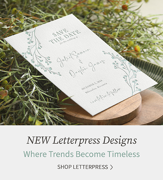 A letterpress save the date with greenery design is shown laying against fresh greenery.